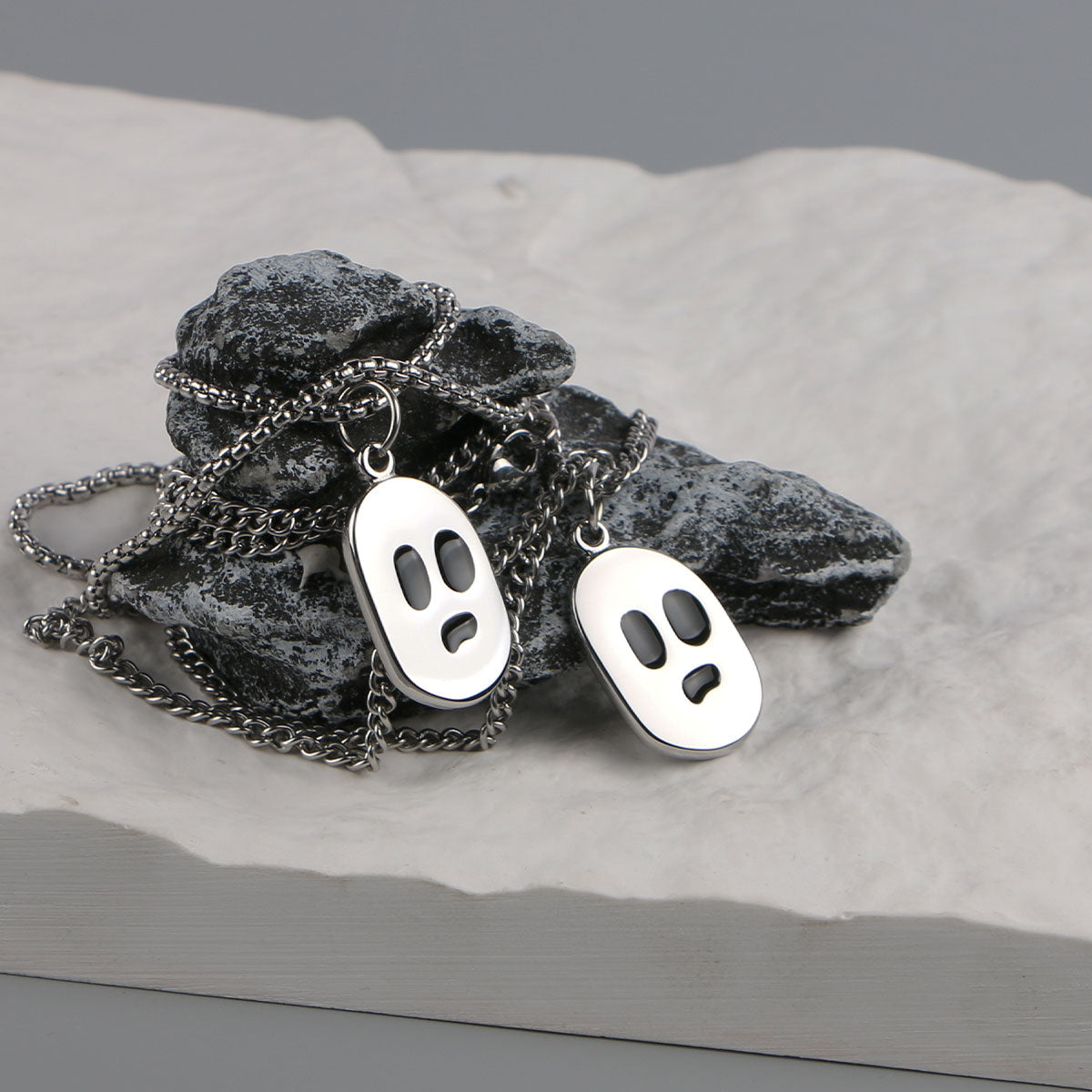 Silver-tone ghost face pendants displayed on dark stones